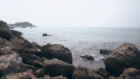 ocean-splashes-on-big-grey-stones-and-distant-water-scooter