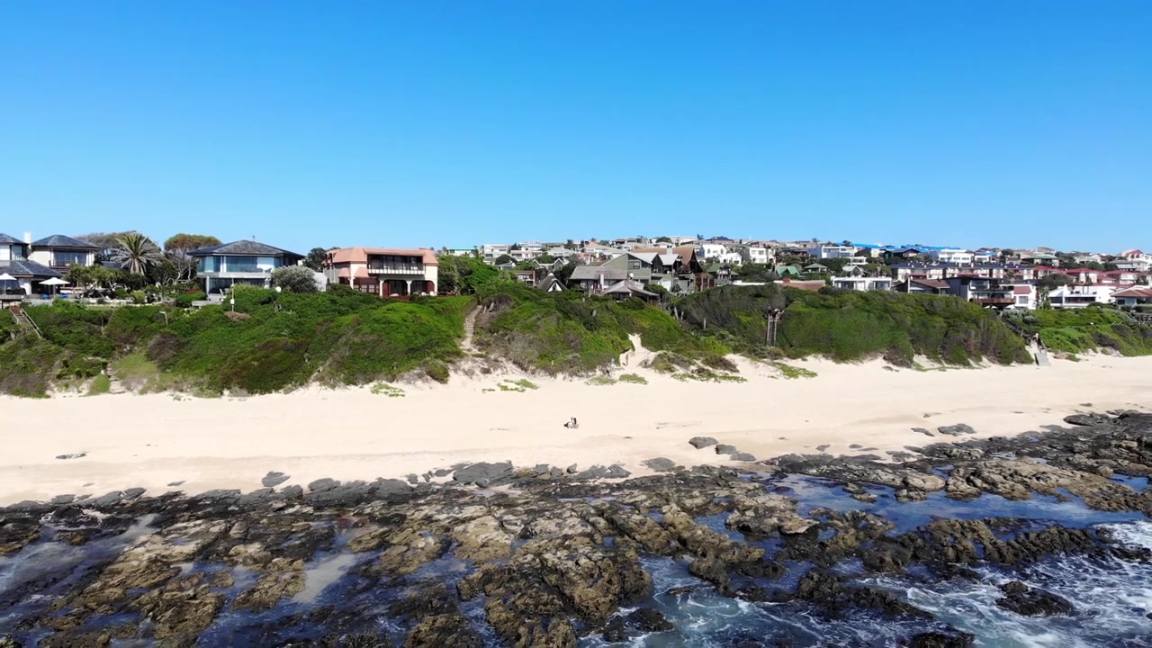 Casal na praia de Jeffreys Bay em dia ensolarado. Aéreo em recuo