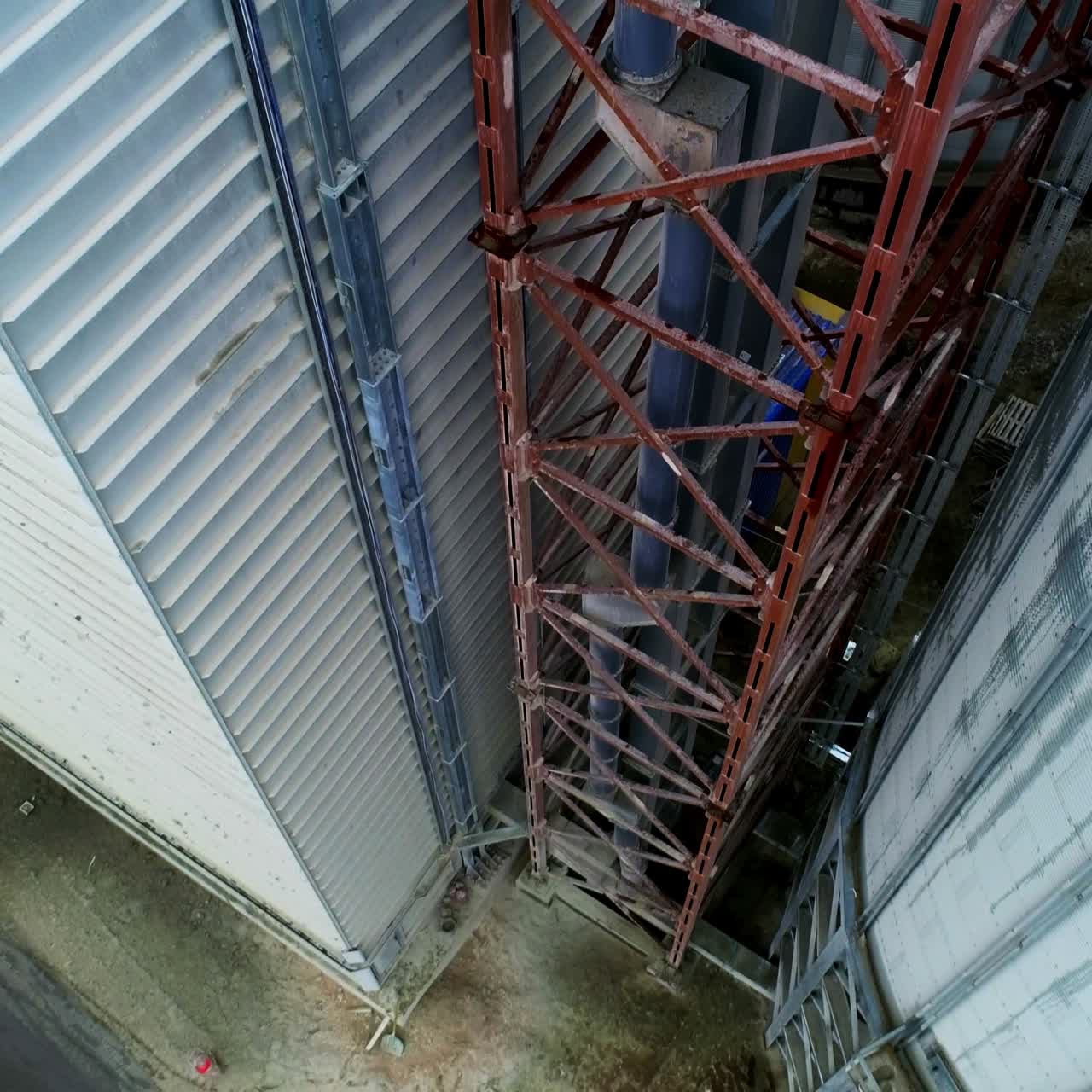 Metal brown tower with tube inside attached to a silo tank and warehouse. Descending footage along the granary premises. Top view