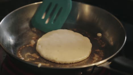 slipping the spatula under the rim of the pancake and lifting it slightly checking the bottom if it is already browned - close up shot