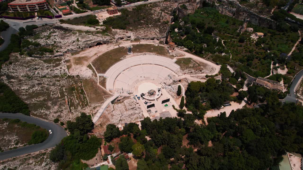 Aerial view of Roman amphitheater in Siracusa, Sicily, surrounded by ruins and Mediterranean greenery