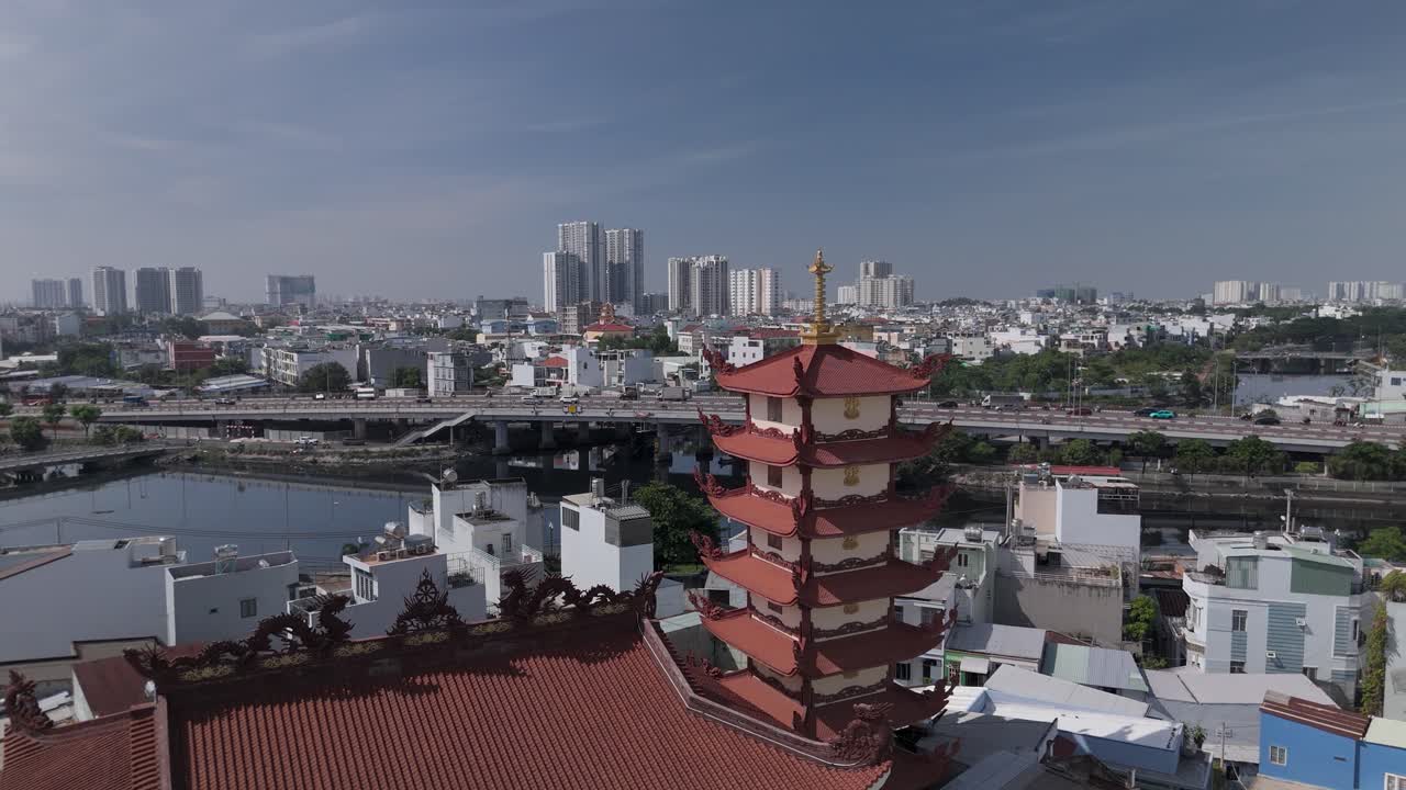Orbit CCW drone view across Buddhist pagoda in busy urban area of Ho Chi Minh City, Vietnam on a sunny clear day featuring transportation infrastructure of main roads and canals in background