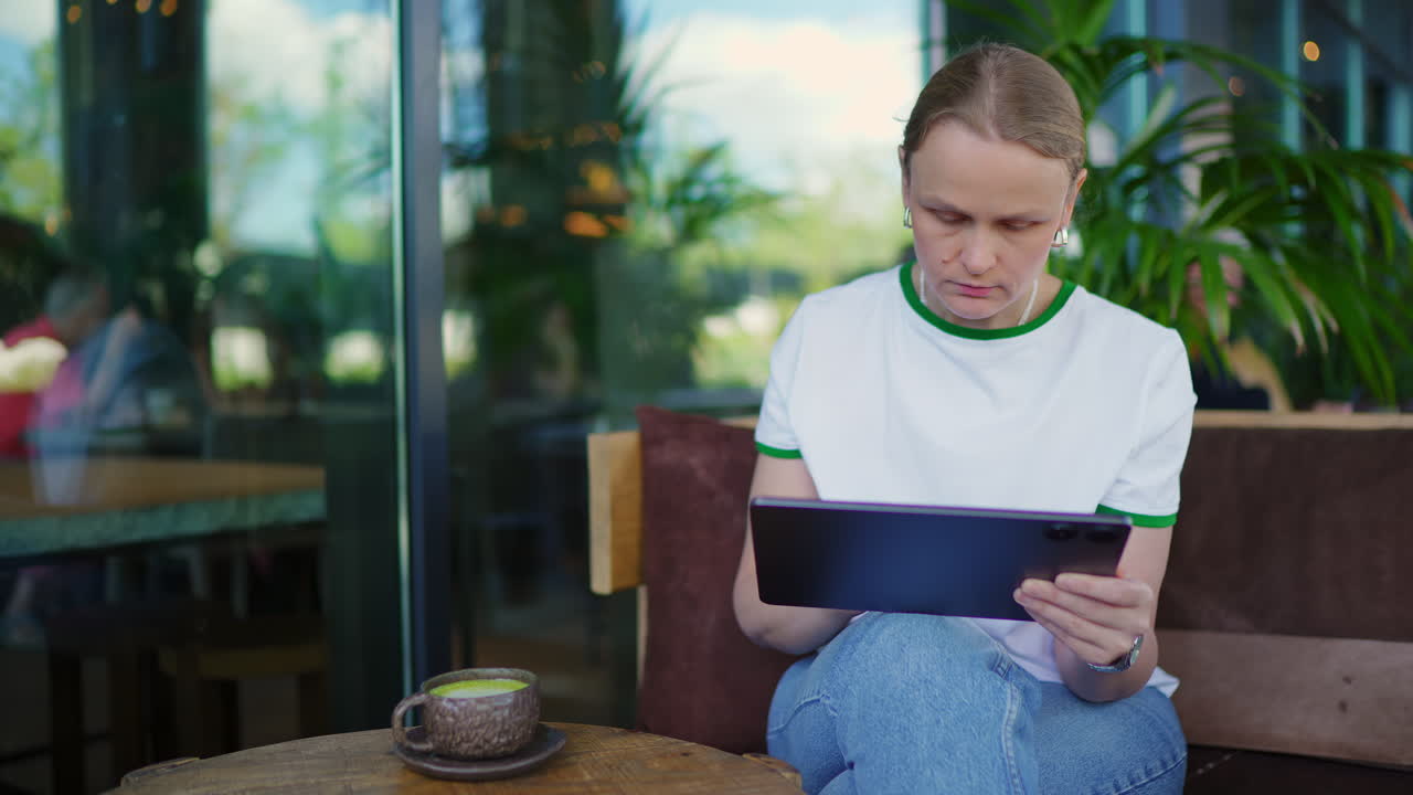Young Woman Drinking Matcha Latte and Using Tablet in Cafe