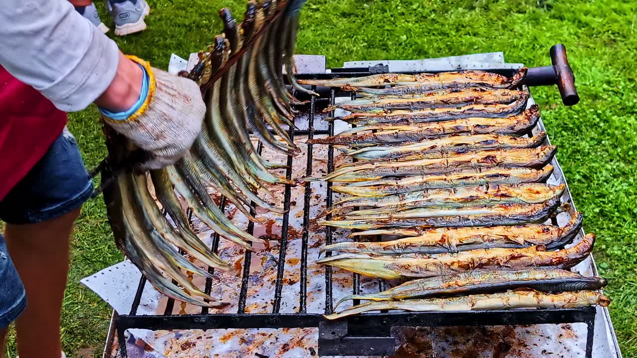 Grilled fish being prepared outdoors on a barbecue by a person in gloves