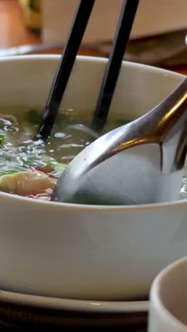 person eating noodle soup with chopsticks and spoon