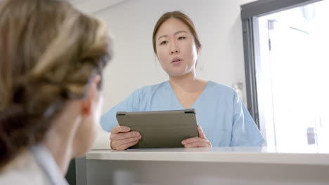 focused diverse female doctors using tablet and discussing over hospital reception desk, slow motion