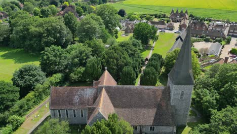 An-aerial-push-in-over-Ickham's-St-John-the-Evangelist-church,-with-the-village-shown-in-the-background