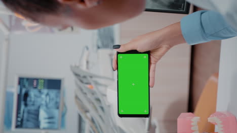 video vertical: mujer sosteniendo un teléfono inteligente con pantalla verde horizontal