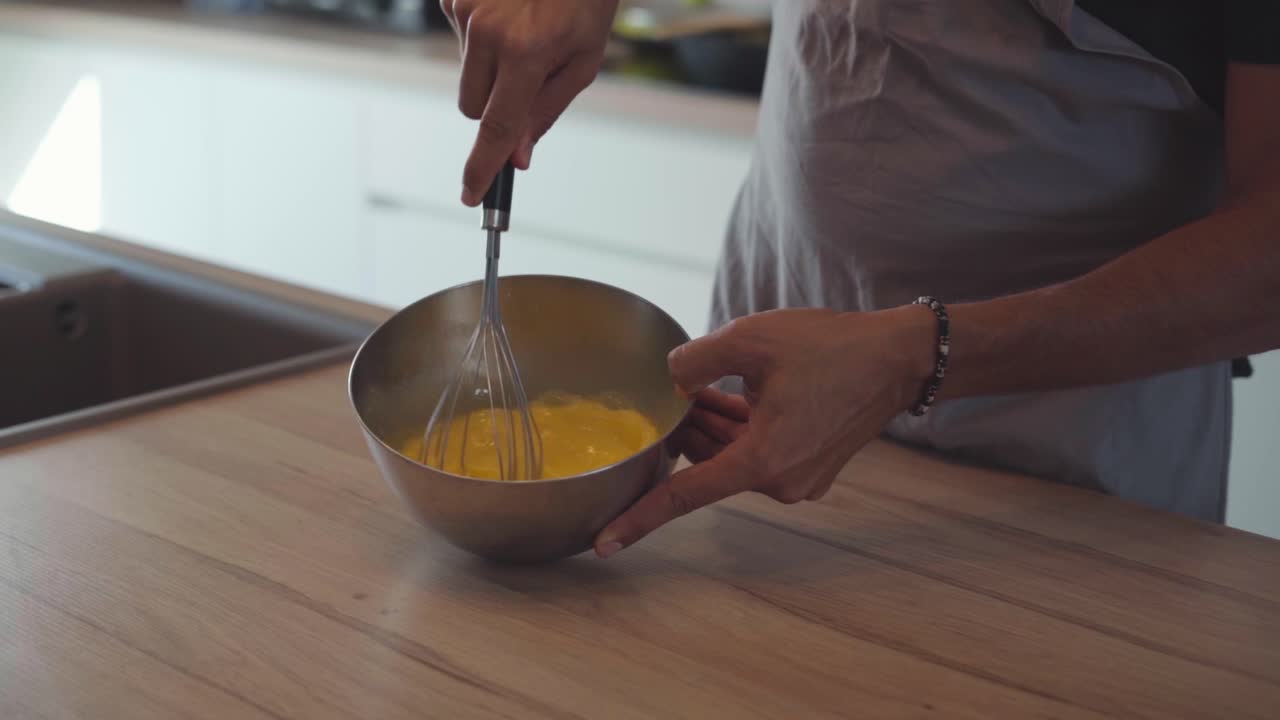 Home professional chef whisking eggs and melted butter in bowl, slow motion