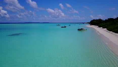 Forward-push-over-brilliant-aquamarine-ocean,-white-sand-beaches-and-fisherman-walking-out-to-boats-in-shallow-waters