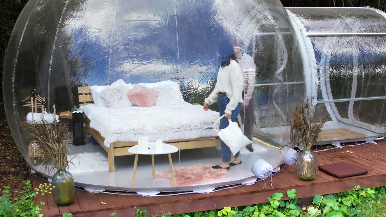 Una coppia che parla, si abbraccia ed entra in una tenda a bolla trasparente in un glamping, vista da un drone. Foresta lussureggiante intorno