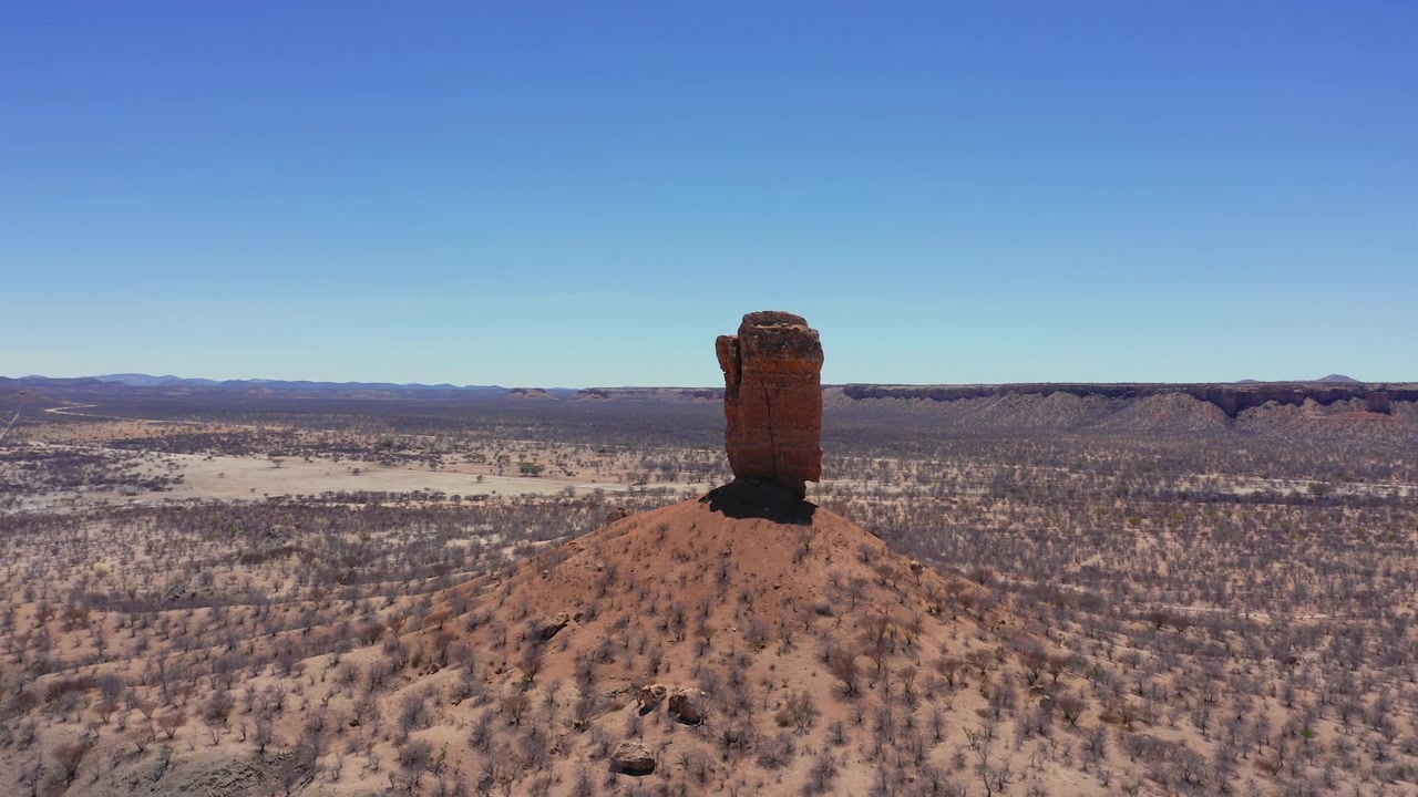 Parlak gün ışığı altında, geniş gökyüzü ve geniş açılı havadan çekimle, kurak Damaraland arazisinin üzerinde yükselen, Namibya'nın 35 metre yüksekliğindeki kaya sütunu Vingerklip'i sergileyen çarpıcı drone çekimi.