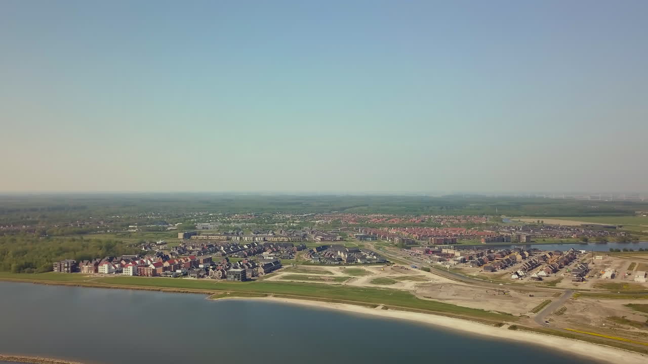 Aerial drone shot of panning to the left over the coastline revealing the suburban and flat landscape in Flevoland, the Netherlands.