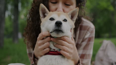 woman affectionately kissing and holding shiba inu dog in park