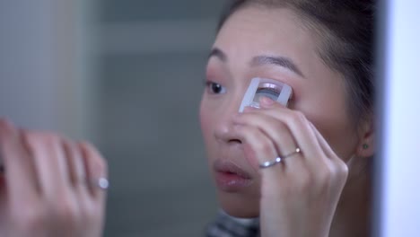 charming ethnic woman using eyelash curler