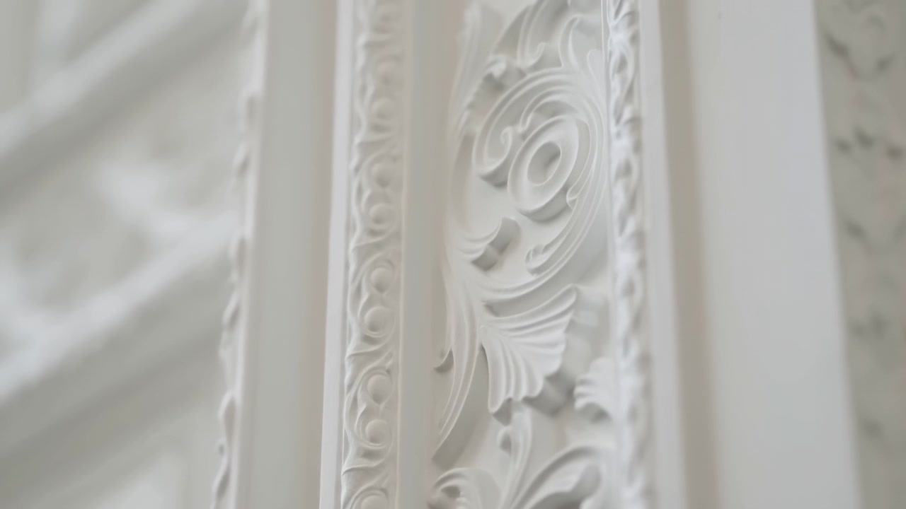 Dettaglio ravvicinato di modanatura in gesso bianca ornata che mostra volute barocche e rilievo intagliato con luce naturale soffusa
