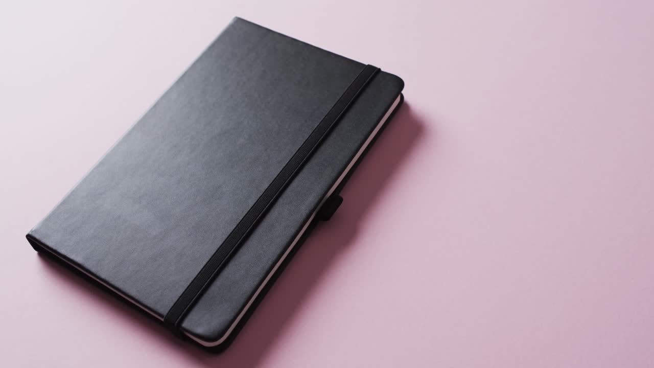 primer plano de un cuaderno negro cerrado con espacio de copia en un fondo rosa en cámara lenta