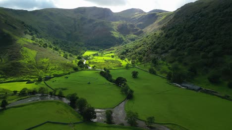 lush green shadowed valley in sunlit pools with farmhouse and mountains beyond