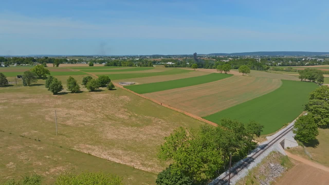 Expansive fields stretch across the landscape under a clear blue sky in Pennsylvania. Lush green areas contrast with dry land, illustrating the beauty of rural farming life.