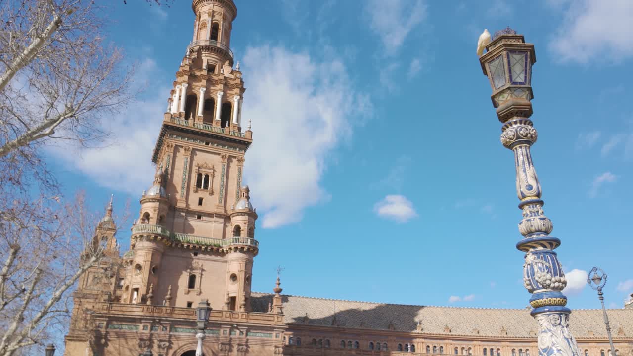Pigeon standing on a decorated street lamp in Plaza de Espana, Seville, Andalusia, Spain, with blue sky and white clouds. pan left