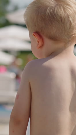 funny little boy with bare chest and shorts walks along large public beach at modern resort on hot summer day close view slow motion