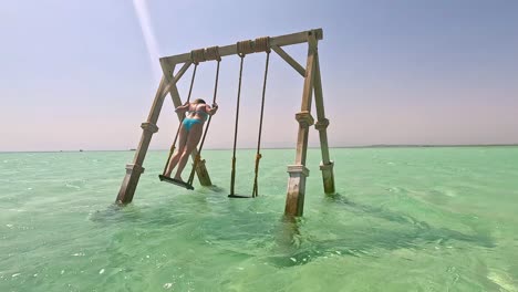 Una-Mujer-En-Bikini-Azul-Claro-En-Un-Columpio-De-Madera-En-Agua-Clara,-Egipto