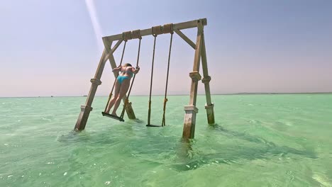 a woman in a light blue bikini on a wooden swing in clear water, egypt