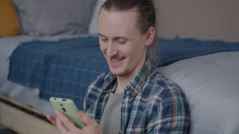 man using a light-green phone in a bedroom
