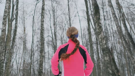 a young woman runs through the park in the winter in a pink jacket. view from the back