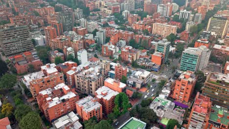 drone shot over dense bogotá with rooftops, buildings, light traffic, roads, and scattered trees.