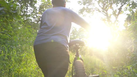 boy man walking toward the sun with a cycle in deep jungle slow motion front camera inspecting looking enjoying view sun light rays flairs in-camera cinematic