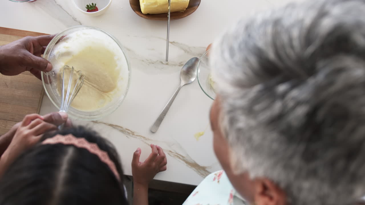 A biracial granddaughter and a grandmother with grey hair are baking together