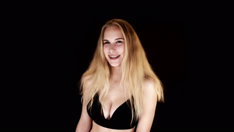 lit from below, a busty blonde woman looks directly at the camera, laughing and shrugging suggestively