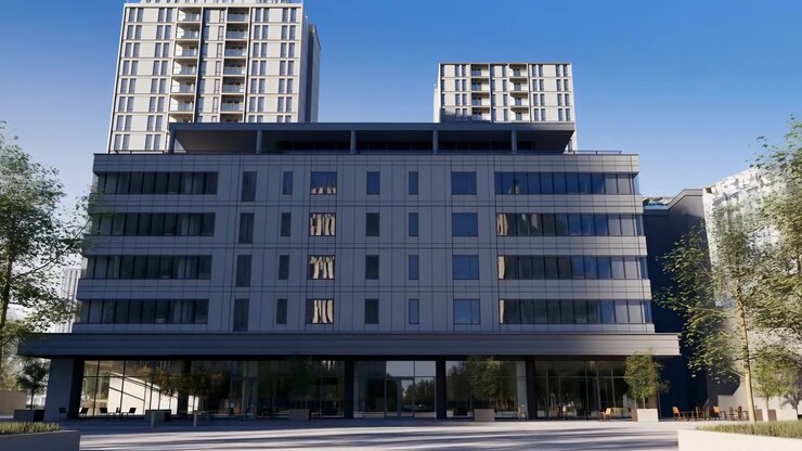 Las sombras se desplazan a través de los paneles rectangulares de la fachada a medida que la vista avanza hacia las entradas de cristal, sillas de exterior y árboles en macetas, con dos torres altas elevándose detrás de un edificio bajo y ancho bajo un cielo azul