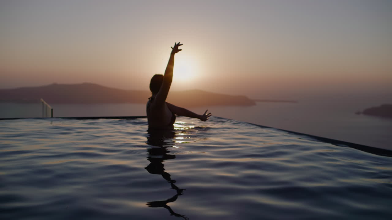 바다 위로 일몰 동안 인피니티 풀에서 춤추는 여성 - 슬로우 모션, 산토리니, 그리스