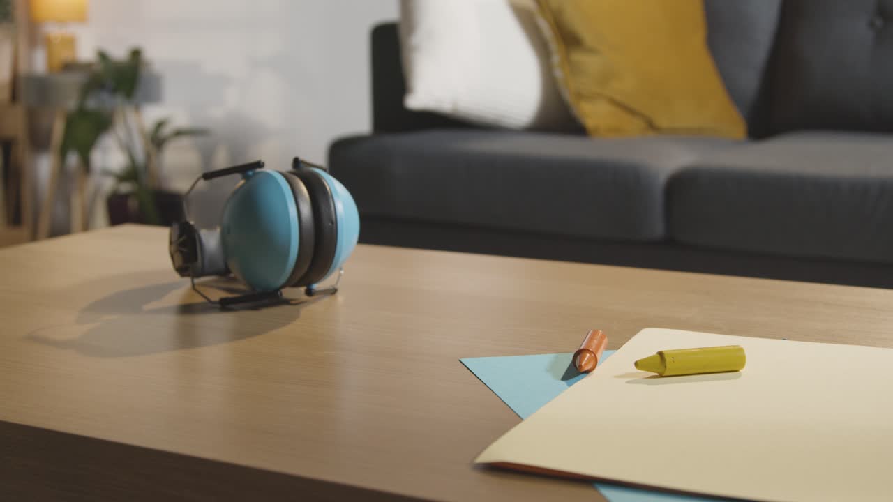 человек, поднимающий ухозащитники со стола с карандашами и бумагой дома для ребенка с диагнозом асд