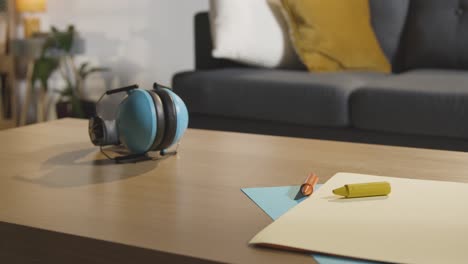 person picking up ear defenders from table with crayons and paper at home for child diagnosed with asd