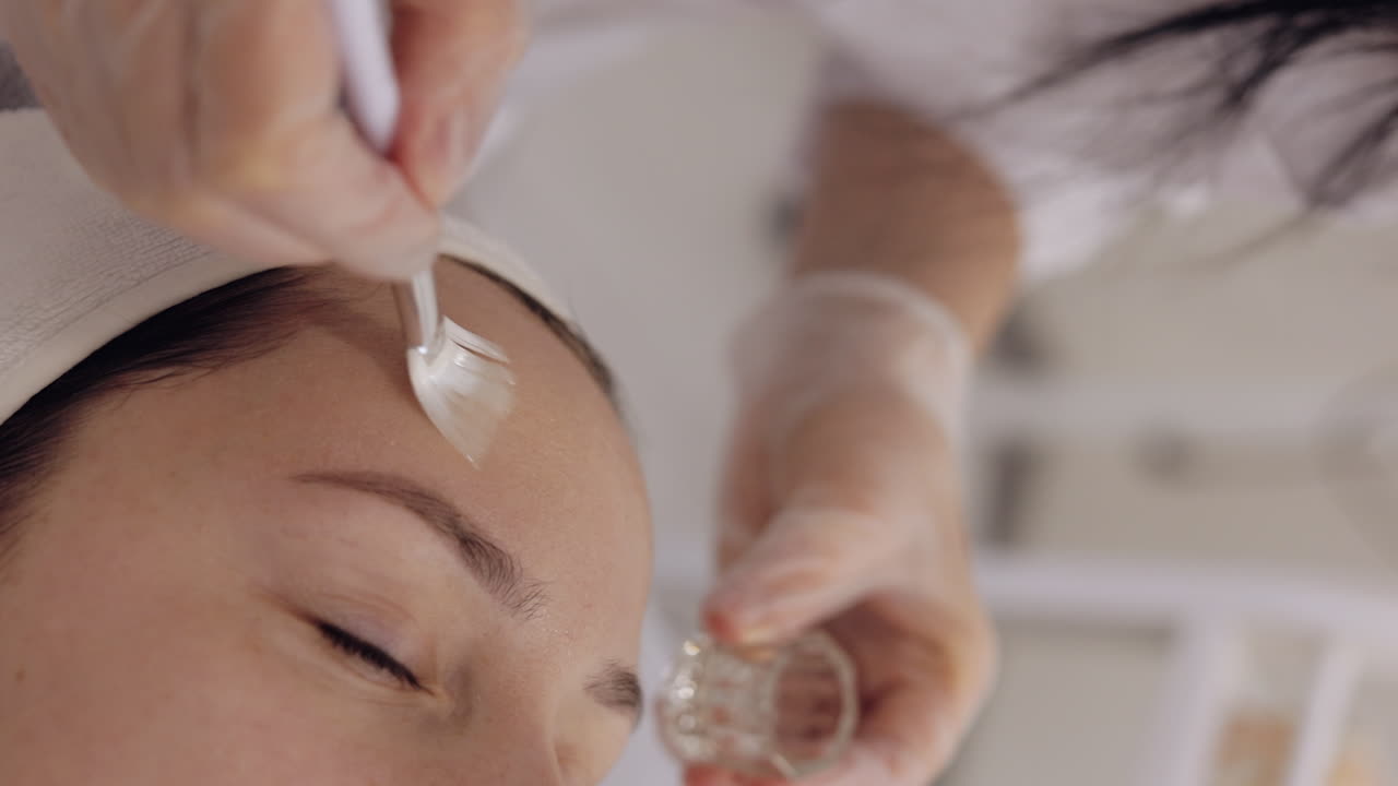 Enzyme therapy beautician applying moisturizing medical cream on middleaged woman face with brushes