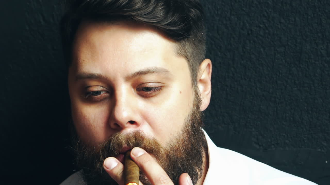 Hombre fumando, perjudicial para la salud. Vista de estudio de un hombre barbudo y con estilo fumando un puro en el estudio.