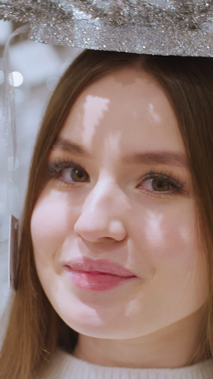 Young woman playfully places sparkling Christmas decoration on her head, surrounded by festive decor in store, enjoying holiday shopping in a beautifully decorated retail environment