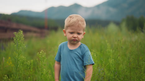 unhappy little boy grimaces walking along meadow grass