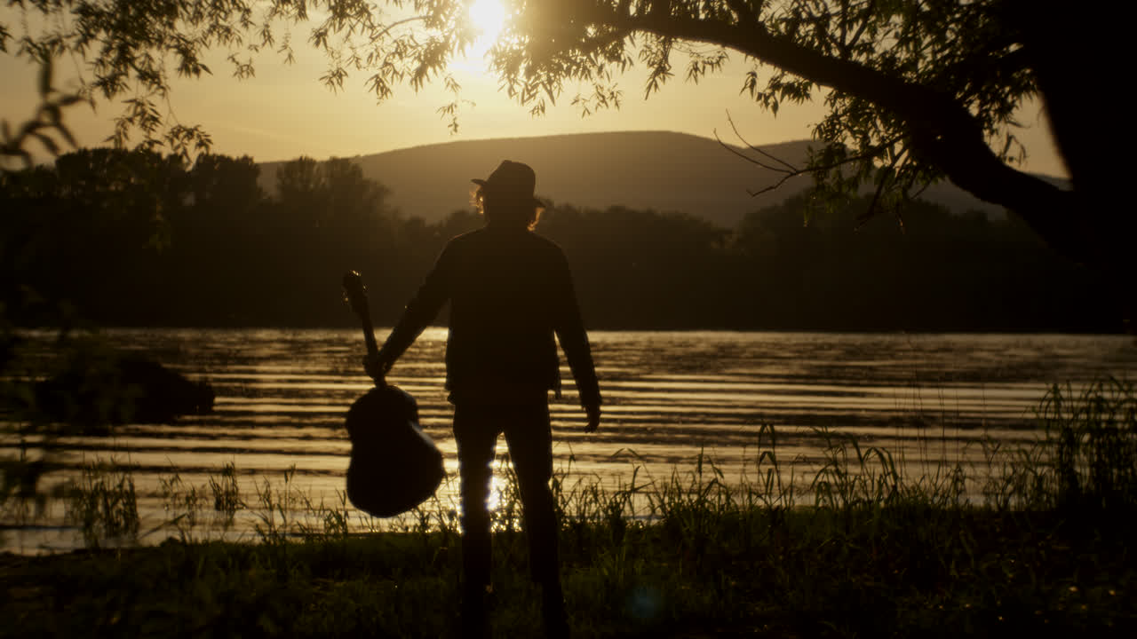 Silhouette of a Man Playing Guitar at Sunset by the River