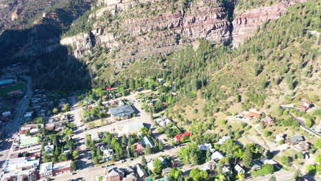 Drone-Aéreo-Inclinado-Hacia-Arriba-De-La-Hermosa-Ciudad-Montañosa-De-Ouray-Colorado-Rodeada-Por-Un-Espeso-Bosque-De-Pinos-Y-Acantilados-Durante-El-Verano-Con-Casas-Y-Automóviles-Conduciendo