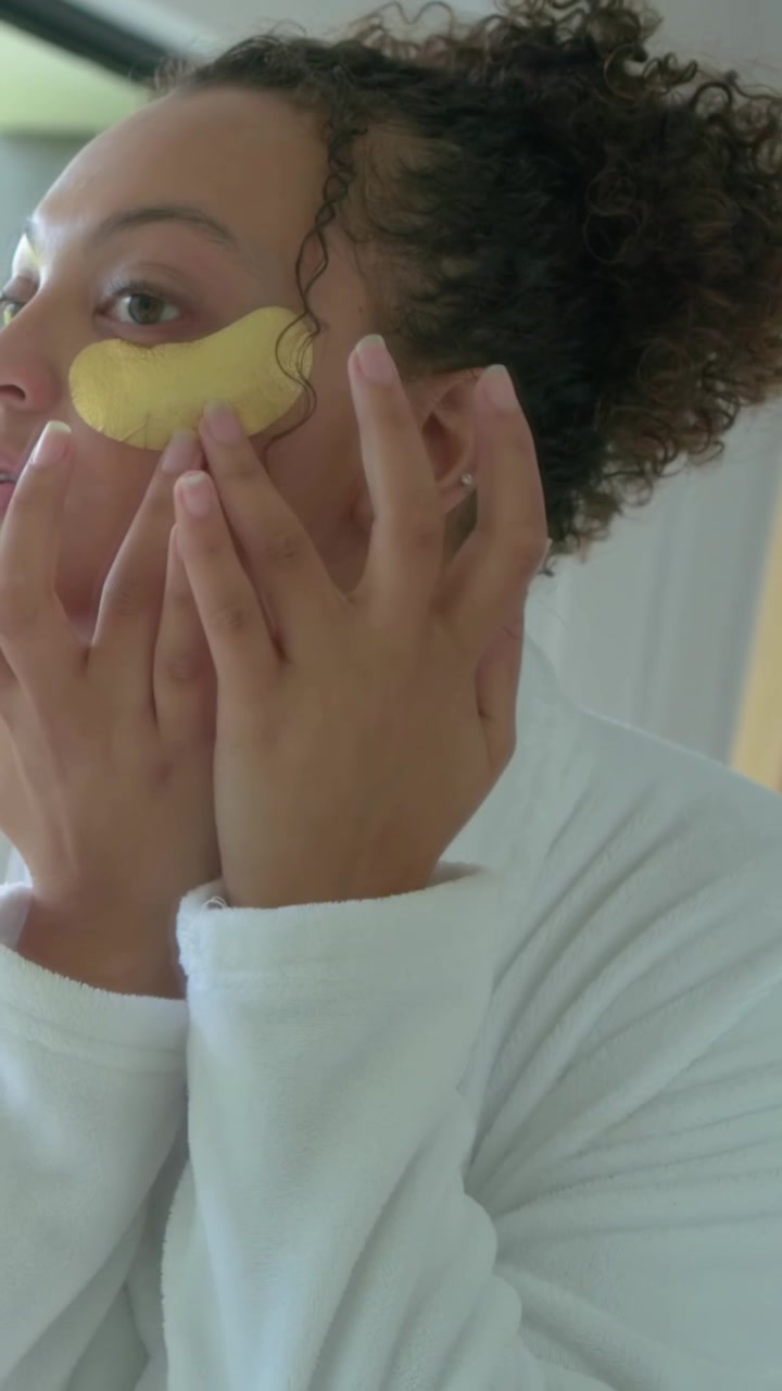 Vertical video: Lifting under eye patch woman applying smoothing at vanity for skincare white robe