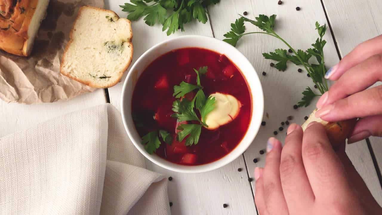 una niña rompe el pan fresco y suave cerca de un plato de sopa de remolacha vegetal
