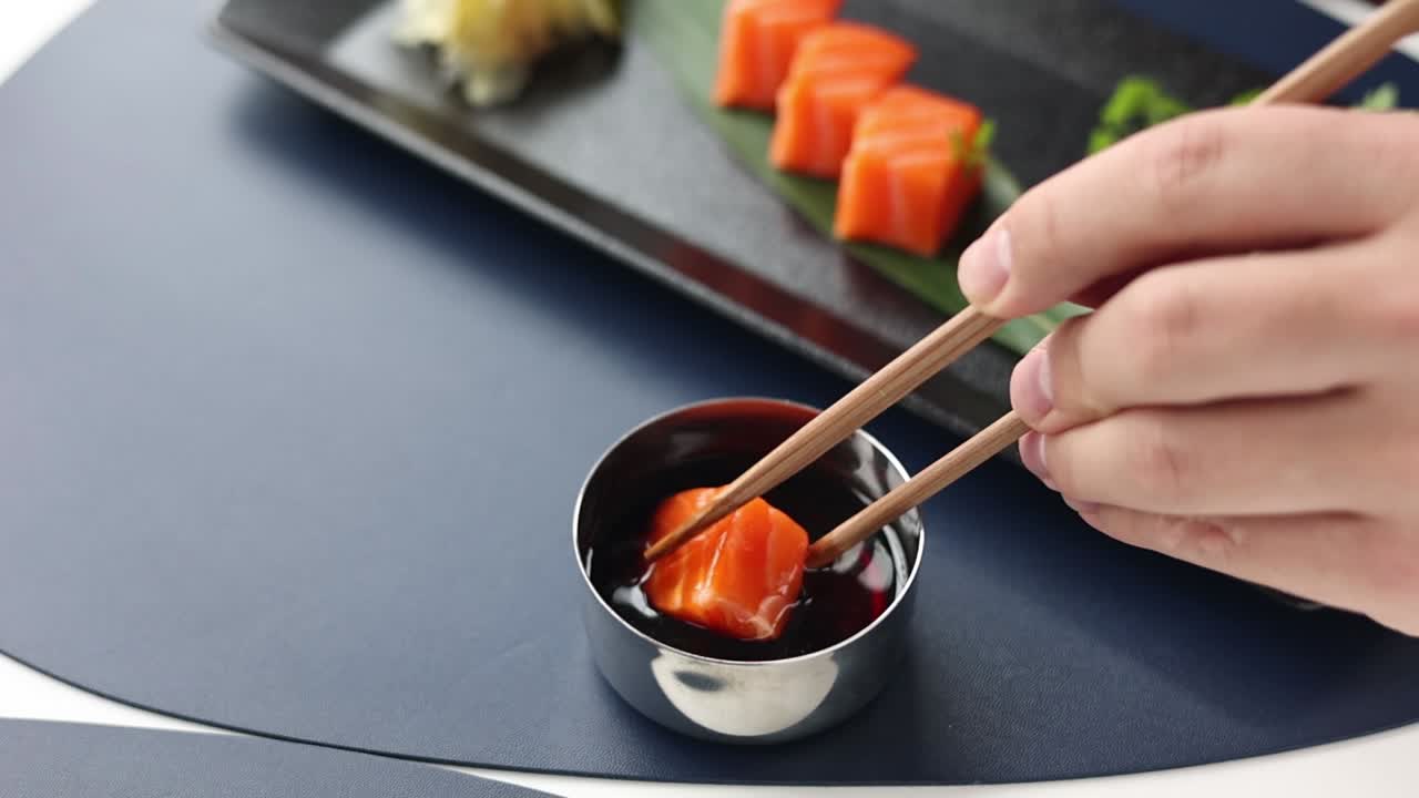 sumergiendo sashimi de salmón con palillos