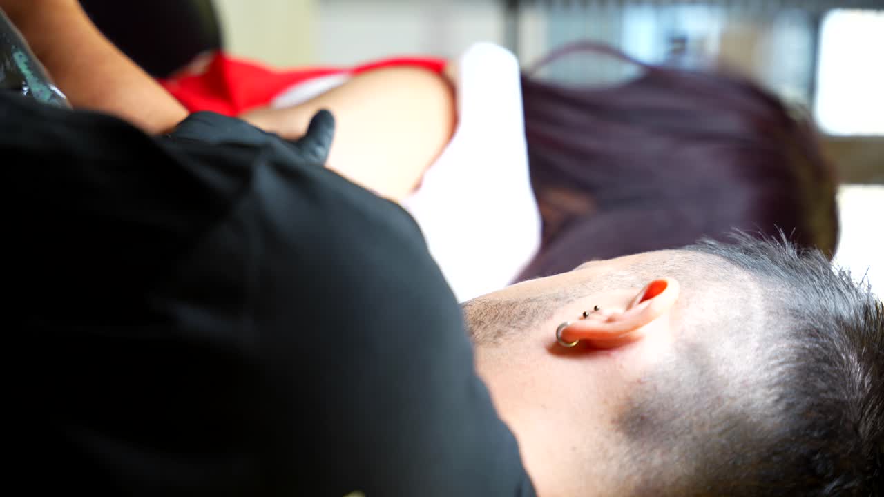 Tattoo artist doing a tattoo on the arm of a woman while checks the design. Vertical shot