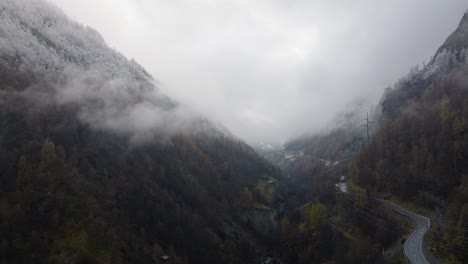 Relaxing-Forward-flying-drone-video-through-cloudy-Swiss-Alps-valley-on-moody-grey-winter-afternoon-with-lush-pine-forests-and-beautiful-snowy-trees-on-mountains-with-road-down-middle-of-the-valley