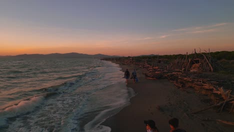 grupo de personas caminando por una idílica playa de arena escénica al atardecer en toscana, italia con carpa tipi de madera a la deriva