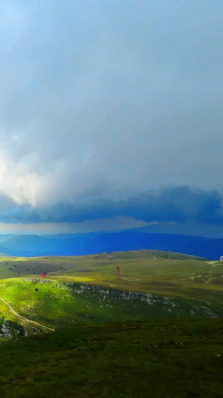 Vista dall'alto di una strada tortuosa nei monti Carpazi, Romania. Autostrada serpeggiante, collina erbosa e cielo tempestoso con luce solare. Video verticale.